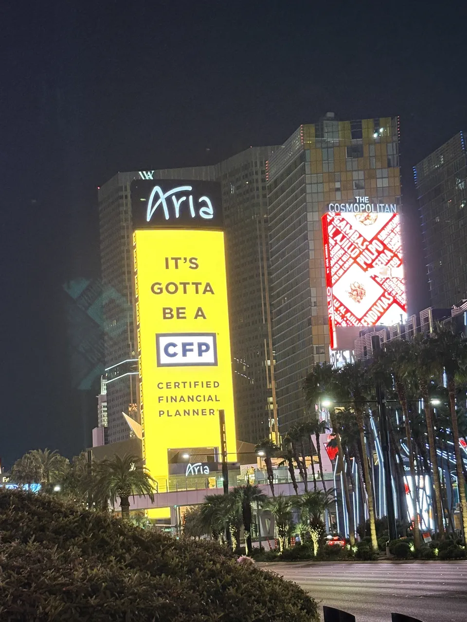 夜里的拉斯维加斯 Aria 酒店，外墙黄色大屏写着 It's gotta be a CFP, Certified Financial Planner